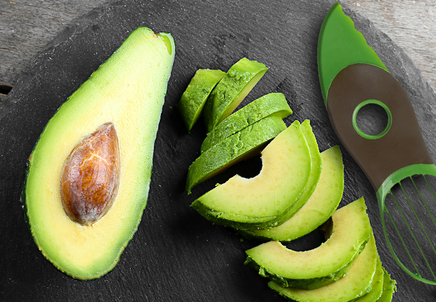 Old El Paso halved avocado with its pit visible beside sliced avocado pieces and a green knife on a slate board.