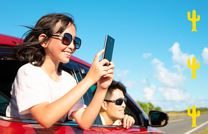People riding in the car looking out the open windows. One person in the back window taking a photo with their phone.
