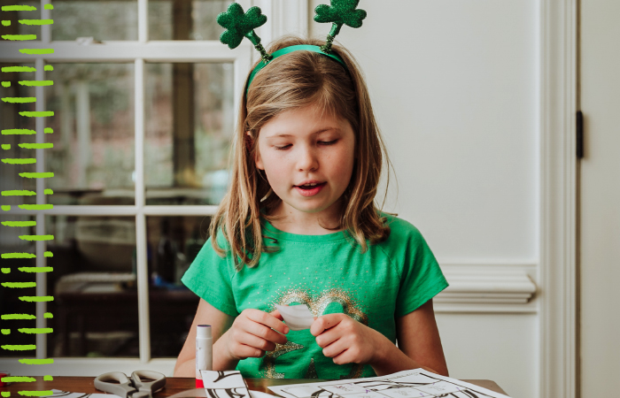 Child wearing a green shirt and a green St. Patricks day headband while doing a craft