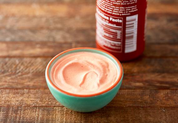 Small bowl of sour cream mixed with hot sauce with the bottle of hot sauce next to the bowl