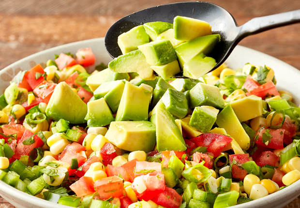 Corn, diced tomatoes, sliced green onion and minced jalapeño mixed in a bowl with diced avocado on top