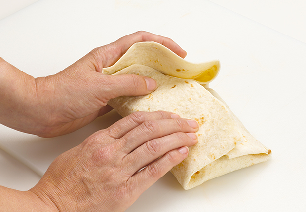 Hands folding over the top part of the burrito