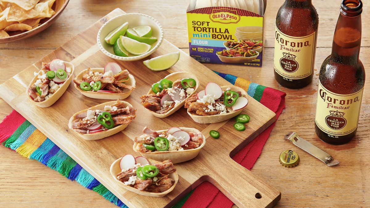 Old El Paso Soft flour Tortilla mini Bowl, front of pack, behind Mini Carnitas Taco Bowls on a wooden board